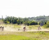 Riders kick up dust as they pedal across the field. © Joe Sales