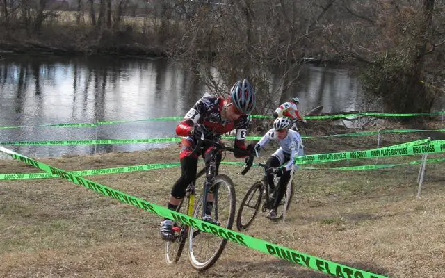 Kat Statman grinds up a short steep hill by the river ahead of Shawn Adams